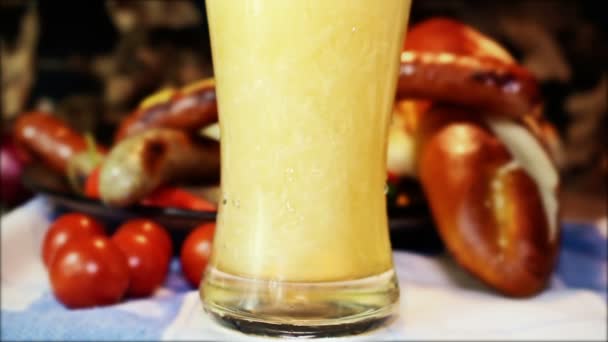 Verser de la bière dans du verre avec le drapeau allemand, des saucisses blanches et rouges bavaroises avec de la moutarde, des pains bavarois et des bretzels à la table en arrière-plan — Video