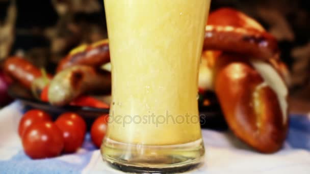 Beer Pouring Into Glass With Waving German Flag and Bavarian White And Red Sausages With Mustard, Bavarian Buns and Pretzels At The Table In The Background. October Fest Concept — Stock Video