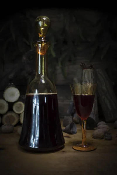 Bottiglia e bicchieri vintage di vino rosso appoggiati sulla tavola di legno sullo sfondo di Natale con tronchi di legno e rami di pino — Foto Stock