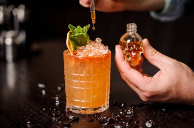 küçük kafatası şeklinde şişe, turuncu kokteyl ve barmen el