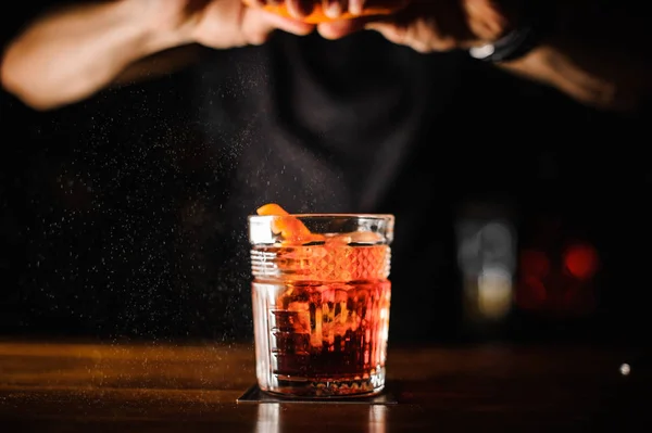 Camarero con vidrio y cáscara de naranja preparando cóctel en el bar — Foto de Stock