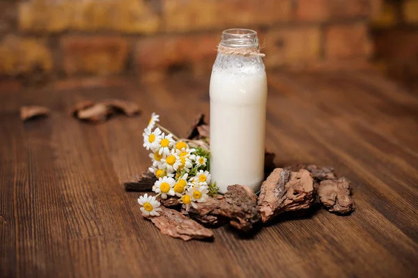 一瓶仿古牛奶和洋甘菊木制的桌子上一束 — 图库照片