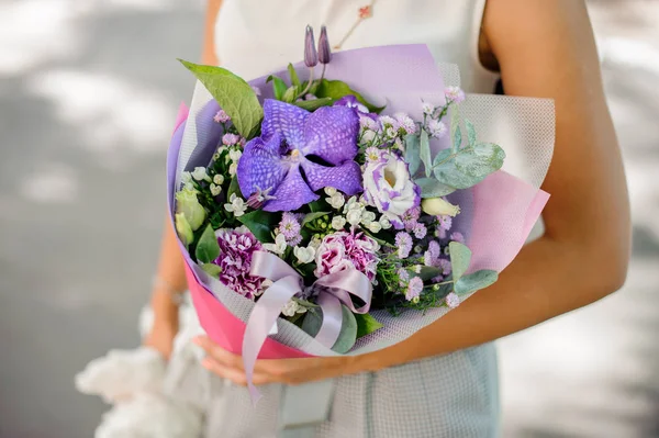 Mãos de mulher segurando uma bela composição roxa de flores — Fotografia de Stock
