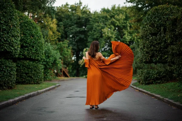 Πίσω όψη του ελκυστική γυναίκα στο μακρύ πορτοκαλί φόρεμα με λουλούδια — Φωτογραφία Αρχείου