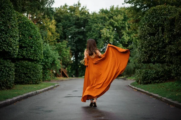 Baksidan på attraktiv kvinna i lång orange klänning stående på vägen — Stockfoto