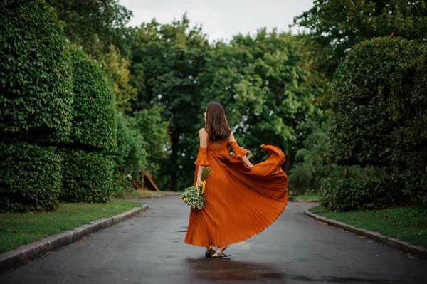 Vista posterior de la hermosa mujer en vestido largo naranja caminando por el camino mojado — Foto de Stock