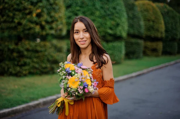 Bir buket çiçek tutan Turuncu elbiseli çekici gülümseyen kadın