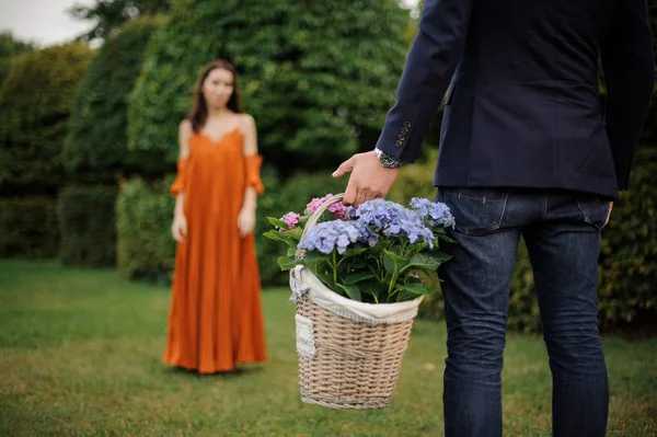 Uomo in giacca e cravatta porta un grande cesto di vimini pieno di fiori per una donna — Foto Stock