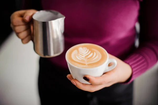 Barista in purple shirt holding a coffee cup with latte art