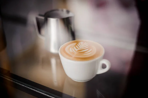 Jarro e xícara de café com bela arte latte na mesa — Fotografia de Stock