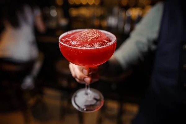 Barista che tiene un bicchiere decorato di cocktail alcolico rosso — Foto Stock