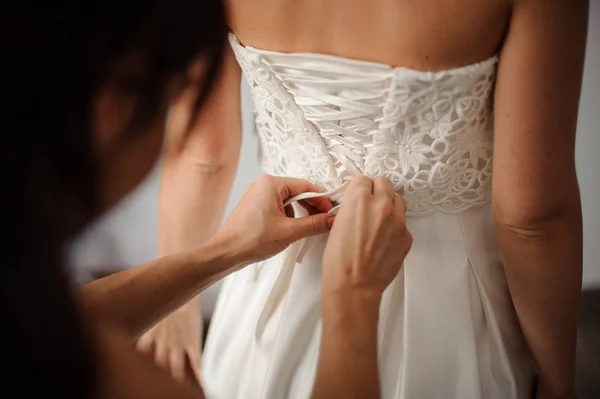 Družička dělá smyčcový uzel na zadní straně nevěsty svatební šaty — Stock fotografie