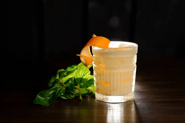 Bebida alcohólica fresca en un vaso decorado con piel de naranja y albahaca — Foto de Stock