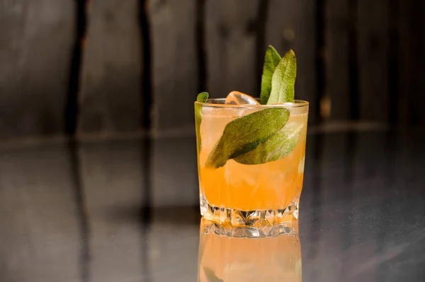 Изолированный стакан апельсинового алкогольного напитка со льдом, украшенный листьями сальвии — стоковое фото