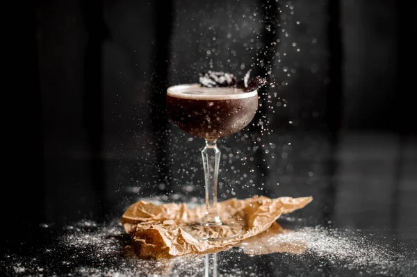 Copa de cóctel con bebida alcohólica oscura espolvoreada con azúcar en polvo y decorada con hojas de albahaca — Foto de Stock