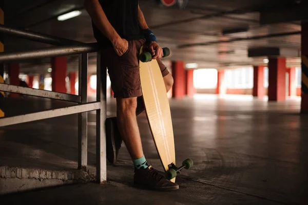 Jovem de calções castanhos segurando um longboard — Fotografia de Stock