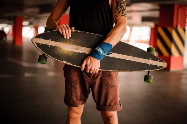 Jovem homem tatuado segurando um longboard em um estacionamento — Fotografia de Stock