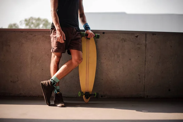 Mladý muž stojící opřený o zábradlí a drží longboard — Stock fotografie