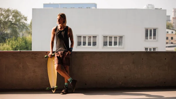 Retrato del hombre de pie con un longboard y mirando hacia otro lado — Foto de Stock