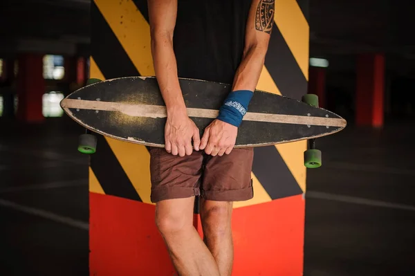 Jovem magro e tatuado cara em shorts marrons com um longboard — Fotografia de Stock