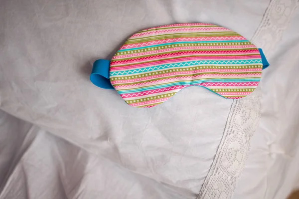 Söta färgglada randiga sovmask på vita sängen — Stockfoto