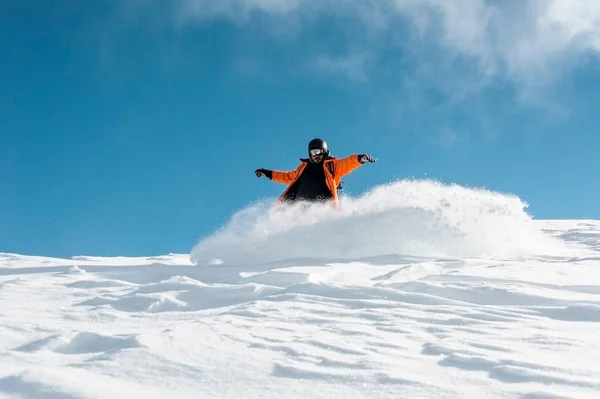 Hombre snowboarder en ropa deportiva naranja brillante cabalgando por la colina de nieve en polvo —  Fotos de Stock