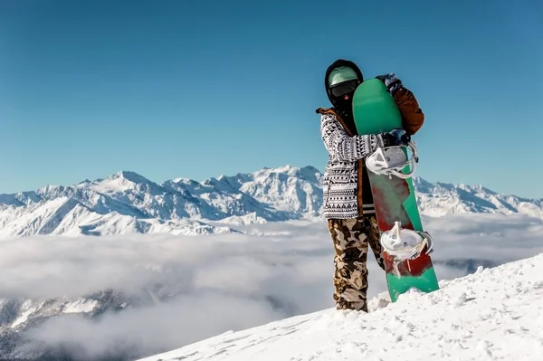Snowboarder αγκαλιάζει το snowboard κατά τις ψηλές βουνοκορφές — Φωτογραφία Αρχείου