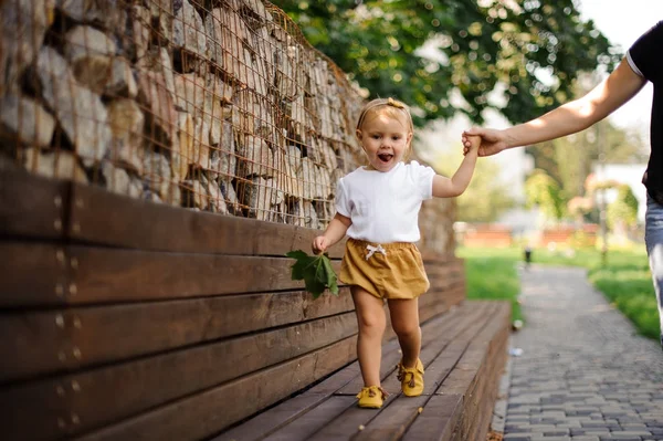 漂亮的小女孩在母亲的手的帮助下走在长凳上 — 图库照片