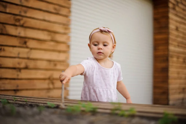 Roztomilá holčička oblečen do pěkně růžové šaty hrát venku s holí — Stock fotografie