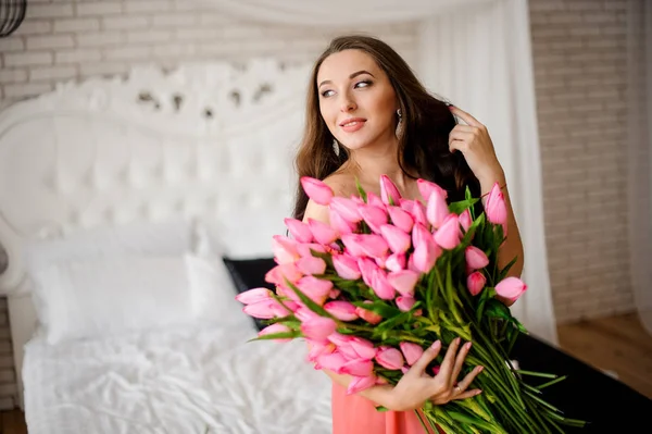 Hermosa mujer de pelo largo sentada en la cama con ramo de tulipanes — Foto de Stock