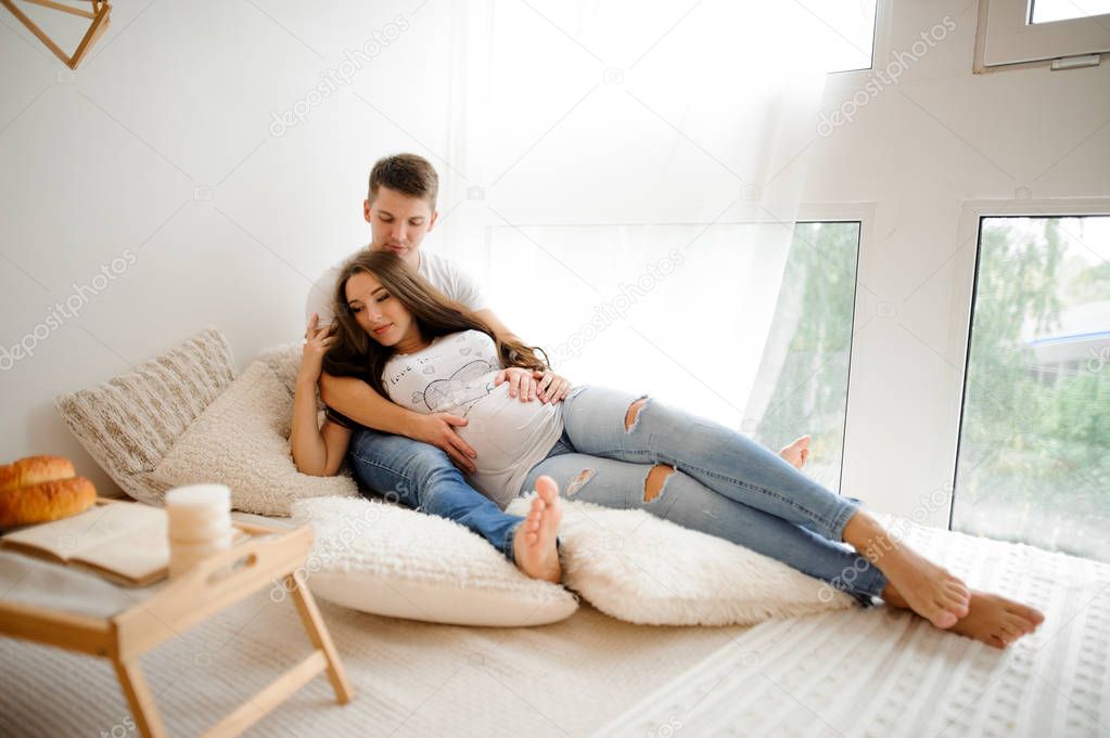Man with beautiful pregnant woman lying on the bed in a white room