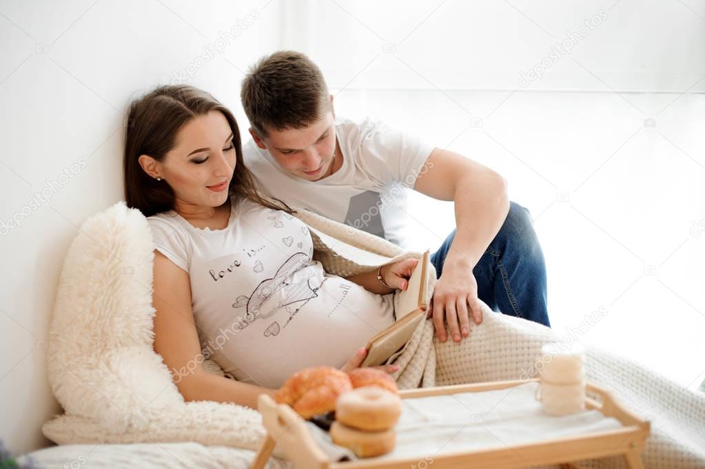 Pregnant woman lying and reading book on the bed with husband
