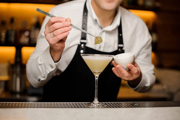 Barmann in weißem Hemd und Schürze dekoriert einen Cocktail mit einem Birkenblatt — Stockfoto