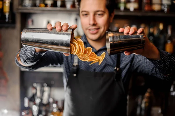 Junger lächelnder Barmann gießt Scheiben frischer Orangenfrüchte ein — Stockfoto