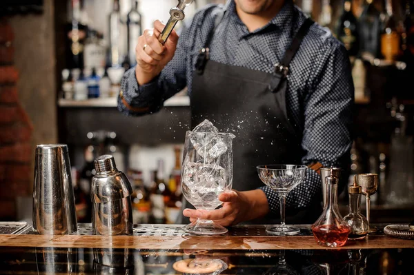 Barman colocando um grande cubo de gelo com a ajuda de pinças de gelo especiais — Fotografia de Stock