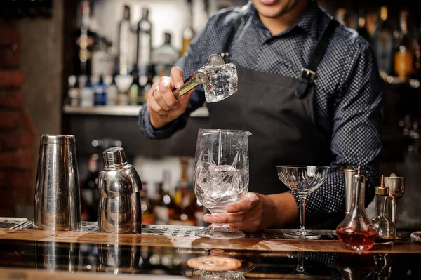 Barista mettere un grande cubetto di ghiaccio nel bicchiere con l'aiuto di pinze di ghiaccio speciali — Foto Stock