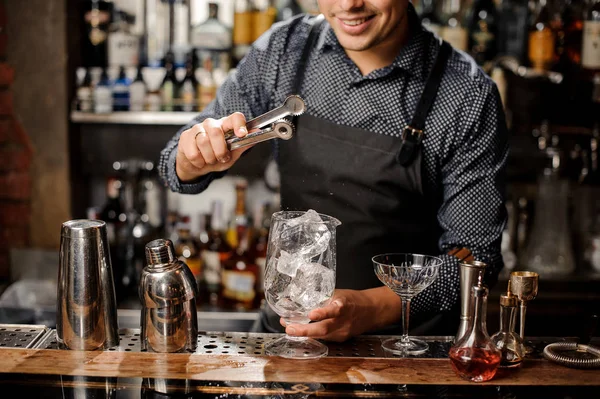 Lächelnder Barkeeper, der mit Hilfe einer speziellen Eiszange einen großen Eiswürfel legt — Stockfoto