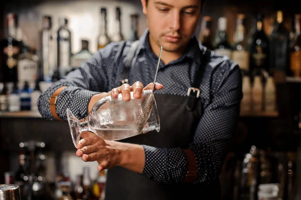 Mladý barman proudí studený alkoholický nápoj z velké skleněné — Stock fotografie