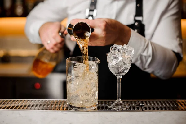 Bartender pouring alcoholic drink into a glass filled with ice cubes — Stock Photo, Image