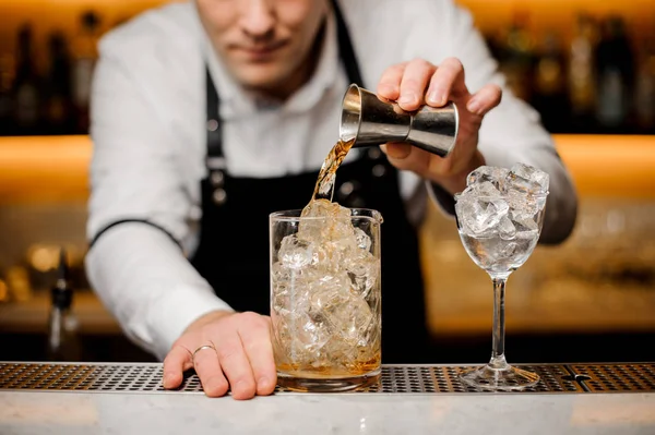 Barman klädd i en vit skjorta hälla alkoholhaltig dryck i ett glas med isbitar — Stockfoto