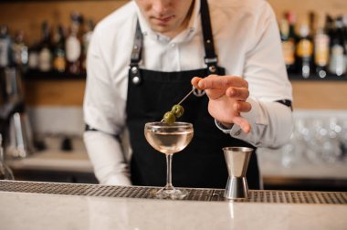 Barmen bir bardak içki ile içine iki yeşil zeytin ekleme