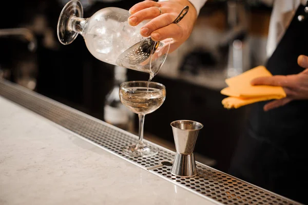 Barman hand pouring alcoholic drink mixed with ice into a glass