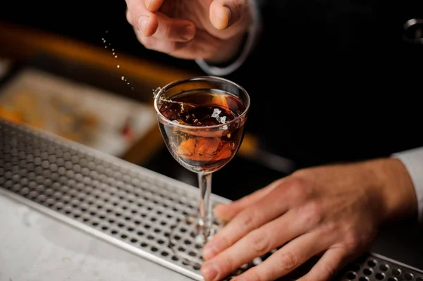 Mano de hombre sosteniendo un vaso con salpicadura de bebida alcohólica con una rebanada de naranja — Foto de Stock