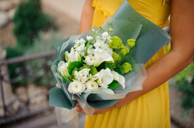 Beyaz ve yeşil bir buket çiçek tutan sarı bir elbise giymiş kız