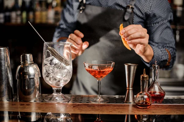 Bartender is going to spray an orange peel in cocktail glass