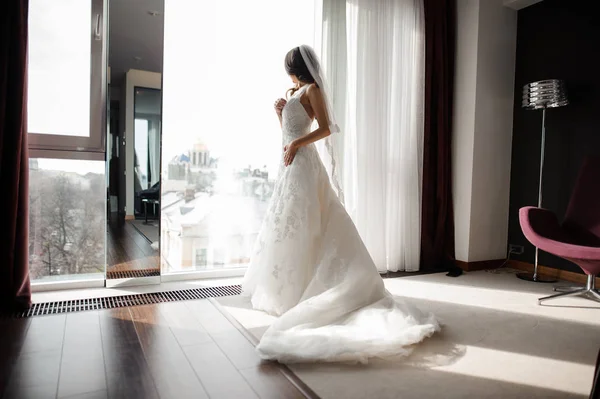 Sposa in pizzo bianco abito da sposa e velo guardando attraverso la finestra — Foto Stock