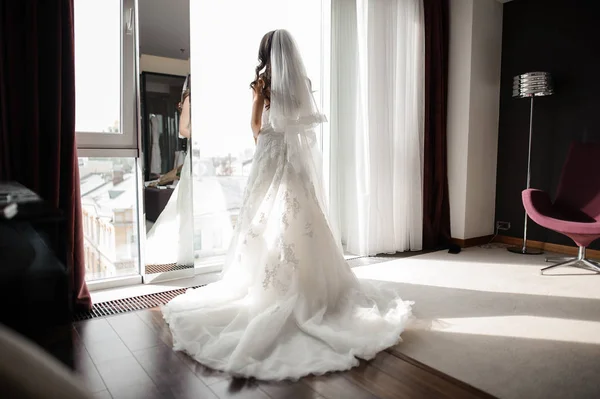 Nevěsta ve svatební šaty a závoj, stojící u okna — Stock fotografie
