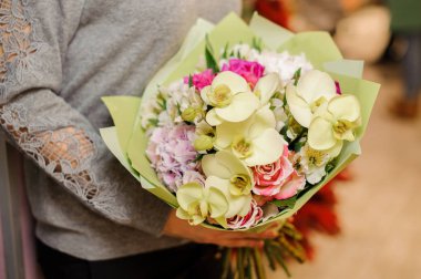kadın bir buket bej orkide, pembe gül ve mor ortanca tutar