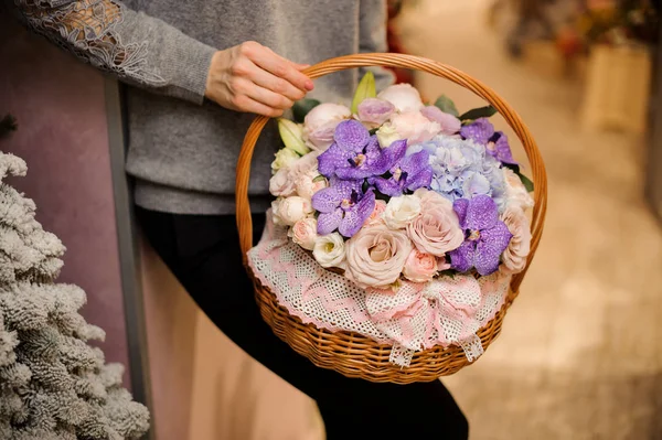 Menina segura uma cesta com orquídeas roxas, rosas rosa e hortênsia azul — Fotografia de Stock