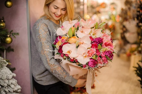 Menina loira sorri e segura um buquê de orquídeas rosa e rosas rosa — Fotografia de Stock